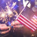 Hands with painted nails hold ignited sparklers and an American flag.