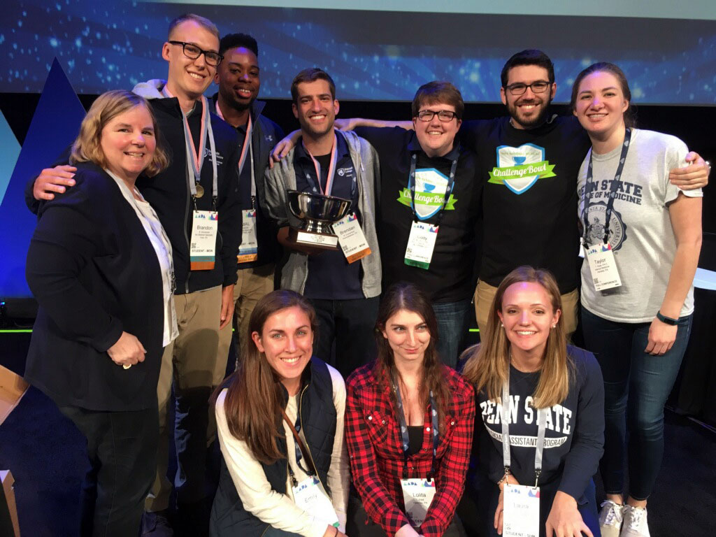 Members of Penn State College of Medicine's physician assistant program National Challenge Bowl team and program alumni and leadership are seen kneeling and standing in a group.