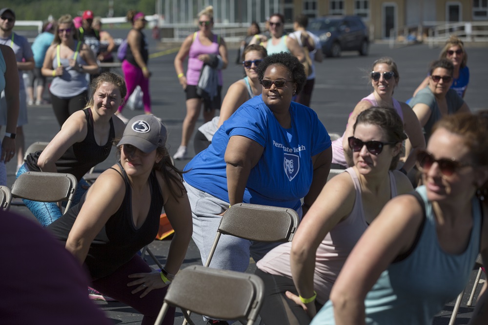 Meghan Culpepper, wearing sunglasses and a Penn State Health T-shirt, joins a group of women all in the same workout position staring at something to the left of the frame.