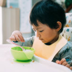 A young child sits at a table with a bowl and a spoon.