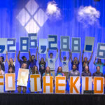 Students hold up poster boards with numbers on them, revealing a fundraising total