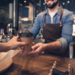 A man hands a woman a cup of coffee over a wooden table.