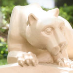 A statue depicting the mascot of Penn State University, the Nittany Lion, surrounded by bushes.