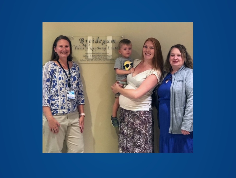 From left, Kimberly Hunter, St. Joseph OB nurse navigator, stands and smiles next to Kelsey Seyler who is holding her two-yer-old son and Sabrina Turner, certified nurse midwife, next to the Breidgam Family Birthing Center sign.