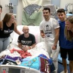 Wearing a Penn State CrossFit shirt and sitting up in a hospital bed, Lily Jordan laughs. Next to her are two women and three young men, the Jonas Brothers.