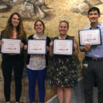 Four students are pictured standing in a row, holding certificates and smiling.