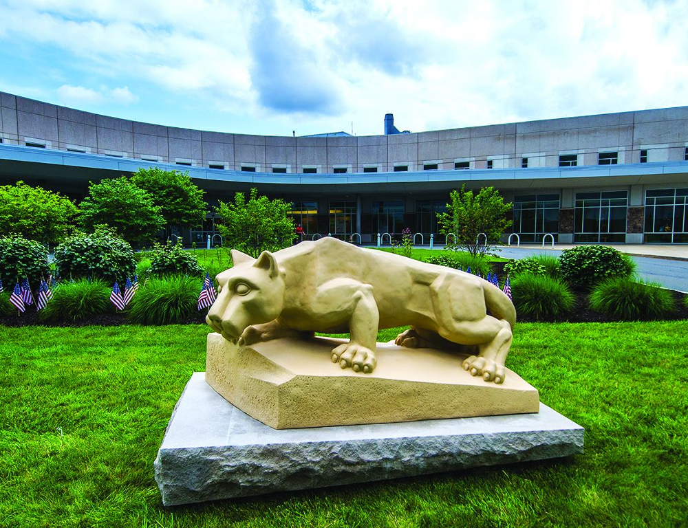 A Penn State Nittany Lion statue is positioned in front of the Penn State Health St. Joseph Medical Center on a grassy lawn lined with trees.
