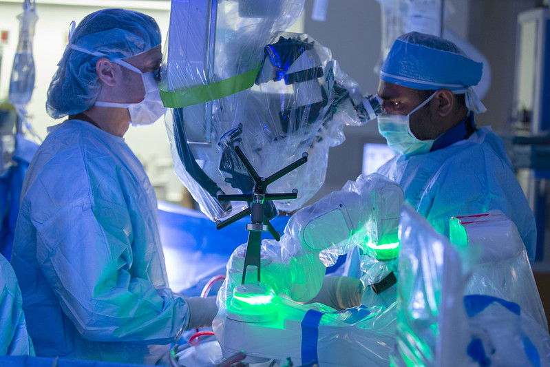 Two people in surgical scrubs look into a robot while performing a surgery