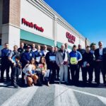 Twenty-one people stand outside a Giant Foods Store. Some hold plaques, flowers and other equipment.