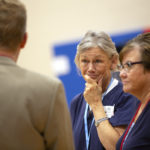 Judy Dillon grips her chin and smiles at a man in a suit.