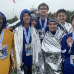 A group of young people wearing marathon numbers, rain gear and medals smile for the camera.