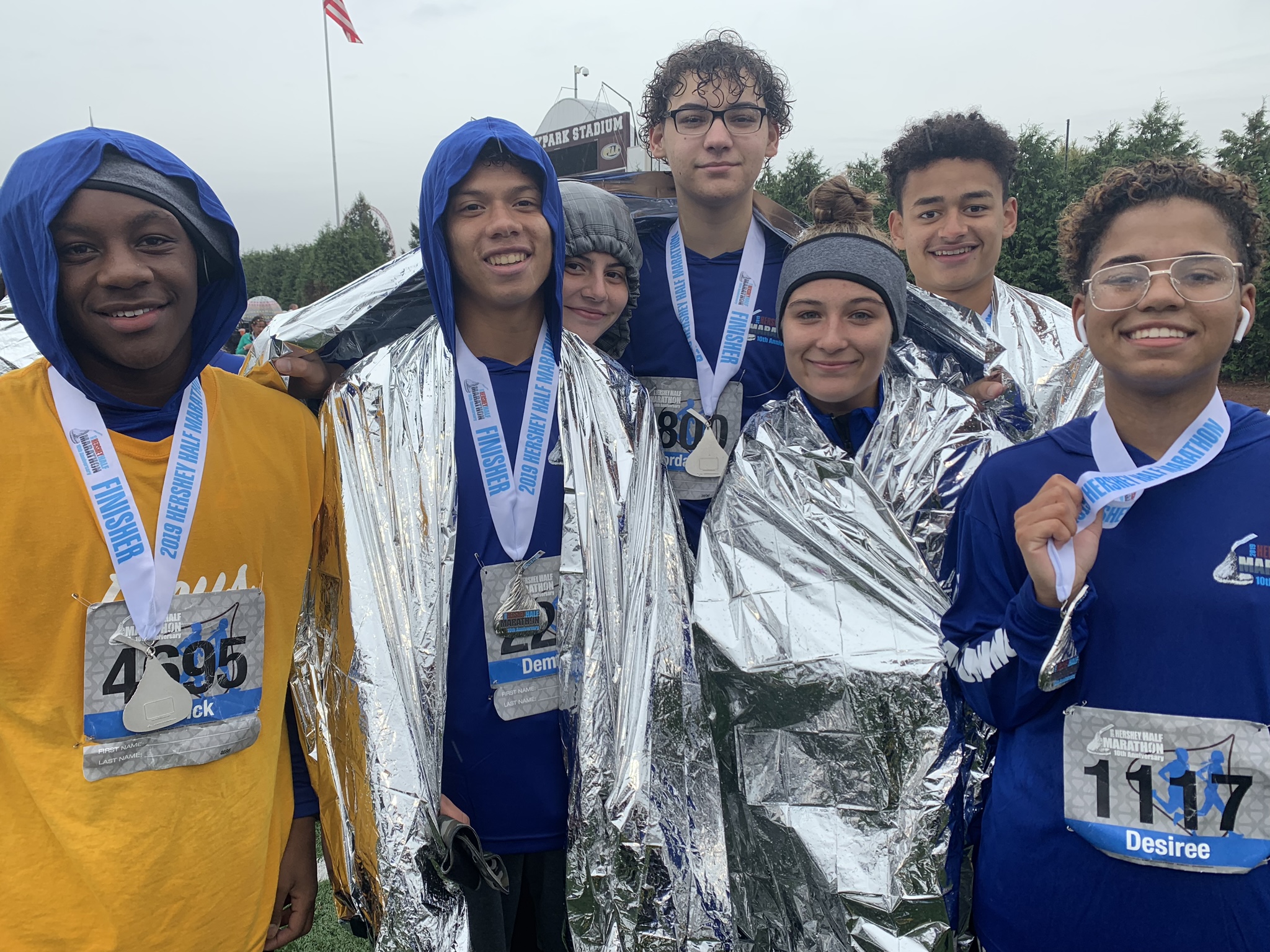 A group of young people wearing marathon numbers, rain gear and medals smile for the camera.