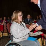 Megan Patrick, wearing a sweatshirt and jeans, smiles at a man in a sport coat who is placing something in her hand. In her other hand, she holds a certificate.