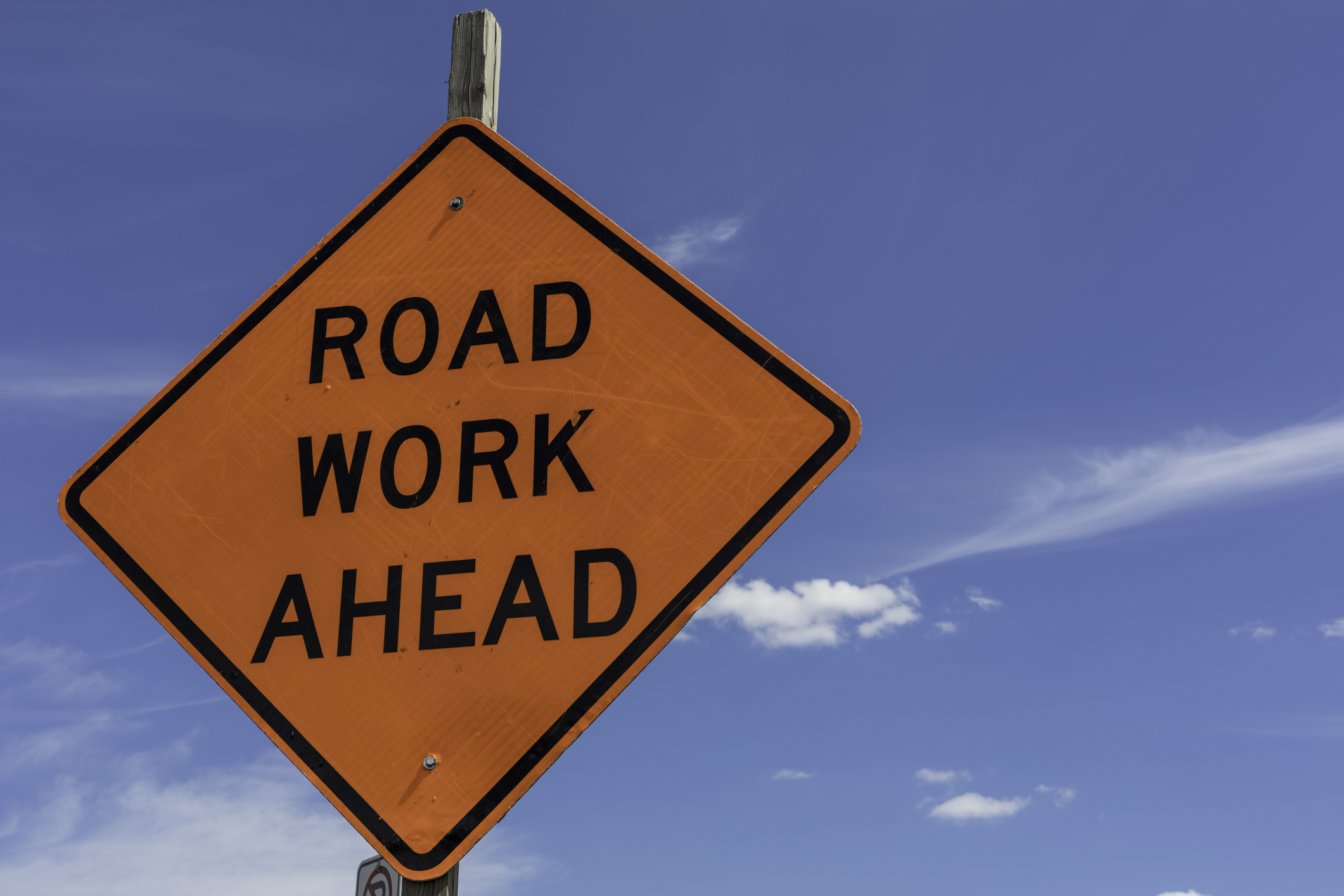 A diamond-shaped roadwork sign stands against a blue sky.