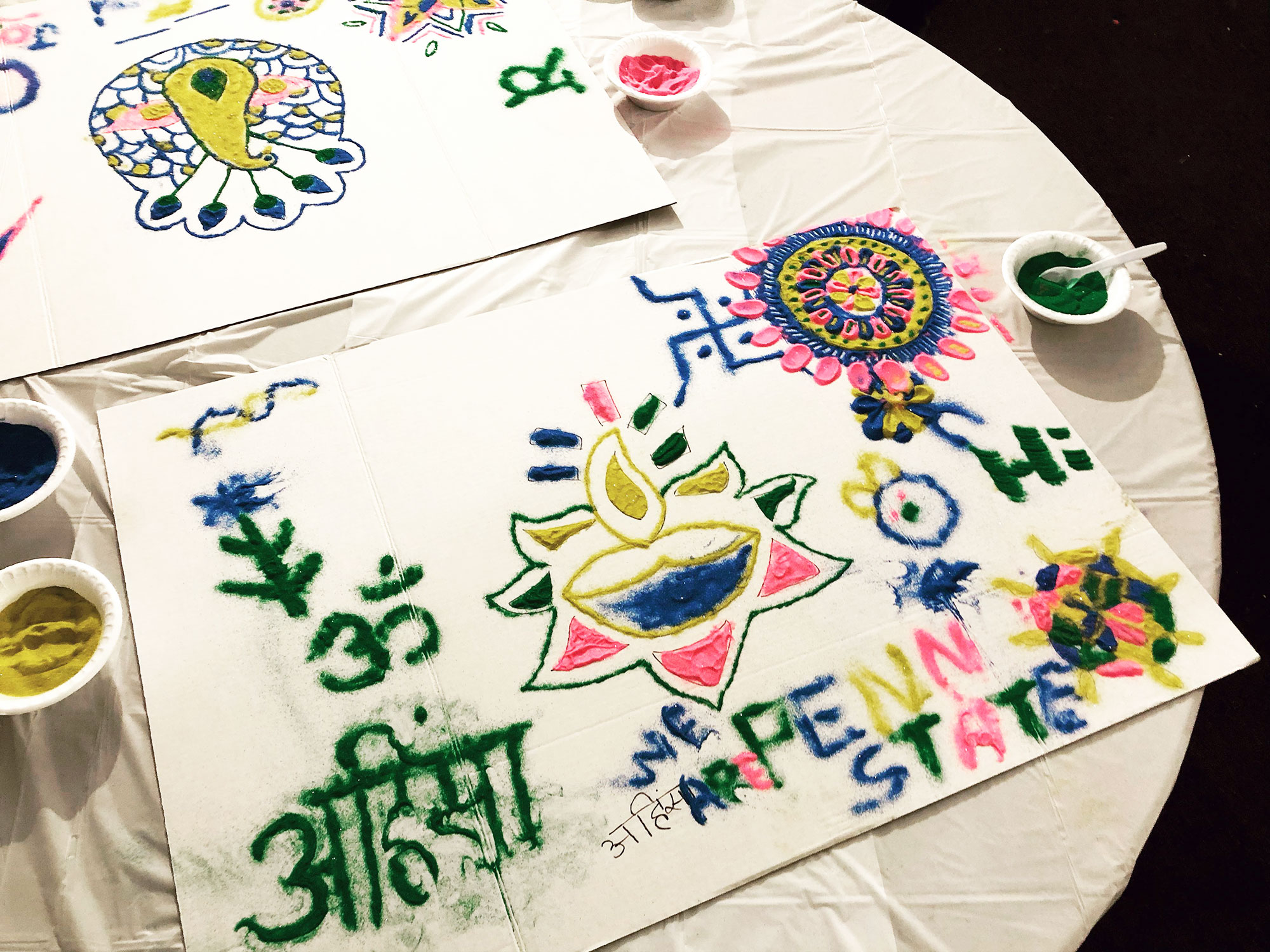 A piece of paper is covered in brightly colored drawings depicting flowers and geometric patterns, as well as the words We Are Penn State and writing in another language.