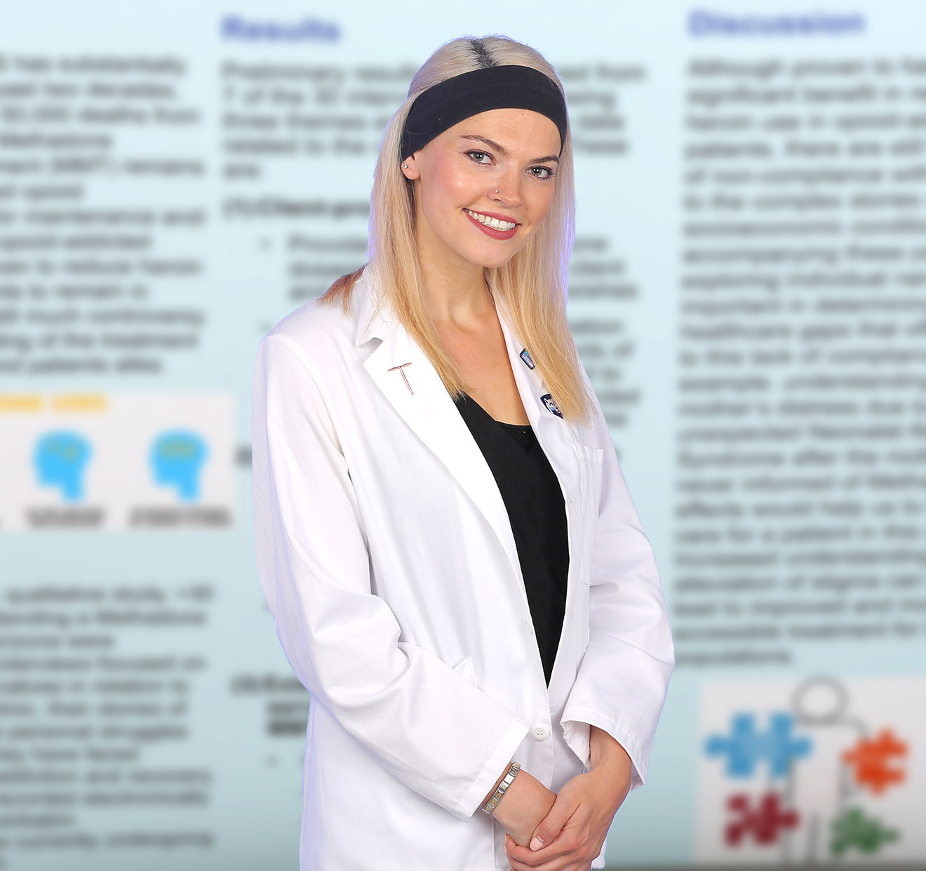 A medical student wearing a medical coat is pictured with an out-of-focus scholarly poster of hers visible in the background.