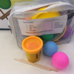 A small plastic bag is seen containing Play-Doh, craft sticks, tape, small balls and more.