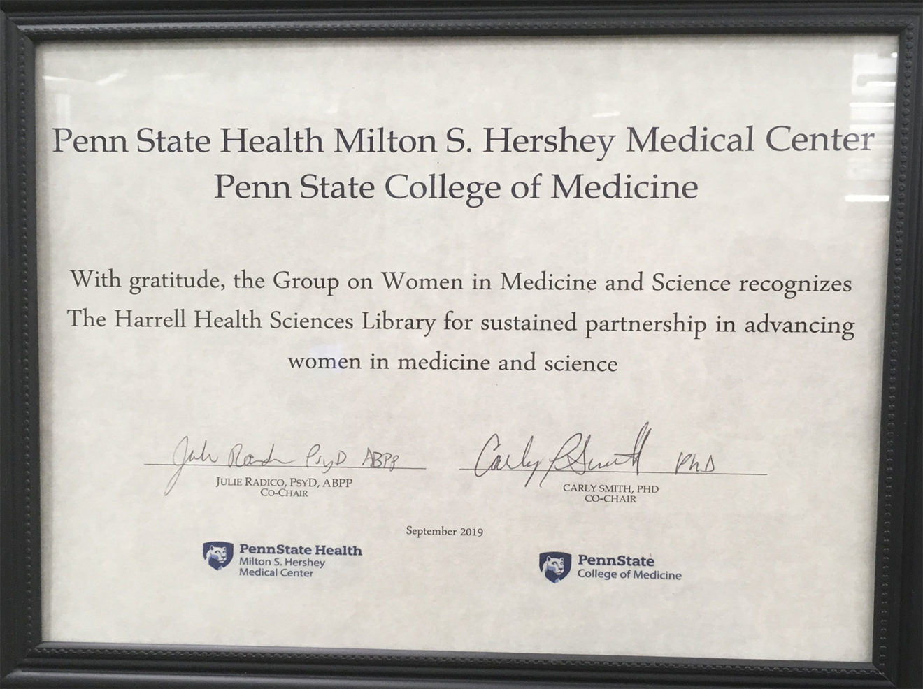 A framed certificate honoring Harrell Health Sciences Library is seen signed by leaders of the Group on Women in Medicine and Science.