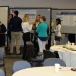 A wide photo shows a number of academic posters in a conference room.