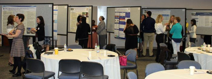 A wide photo shows a number of academic posters in a conference room.
