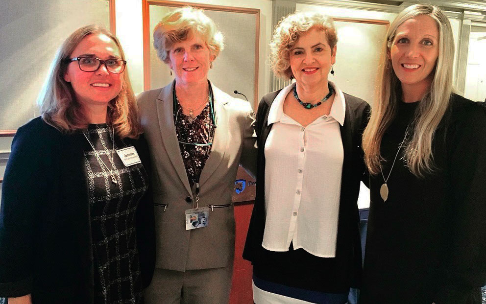 Four women are steen standing in a row with their arms around each other's backs.