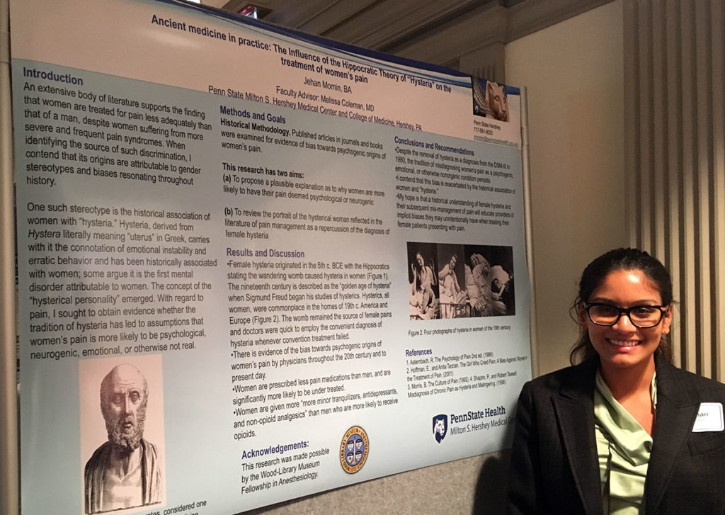 A woman, Jehan Momin, stands in front of an academic poster, smiling.