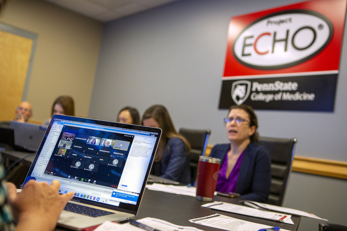 Several people sit around a conference table, on which there are papers, pens and computers. A sign on the wall bears the Project Echo and Penn State College of Medicine logos.