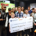 A group of men, women and children gather around an oversized check for $751.52 made out to Children’s Miracle Network.