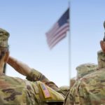 U.S. soldiers are shown from behind saluting a U.S. flag.