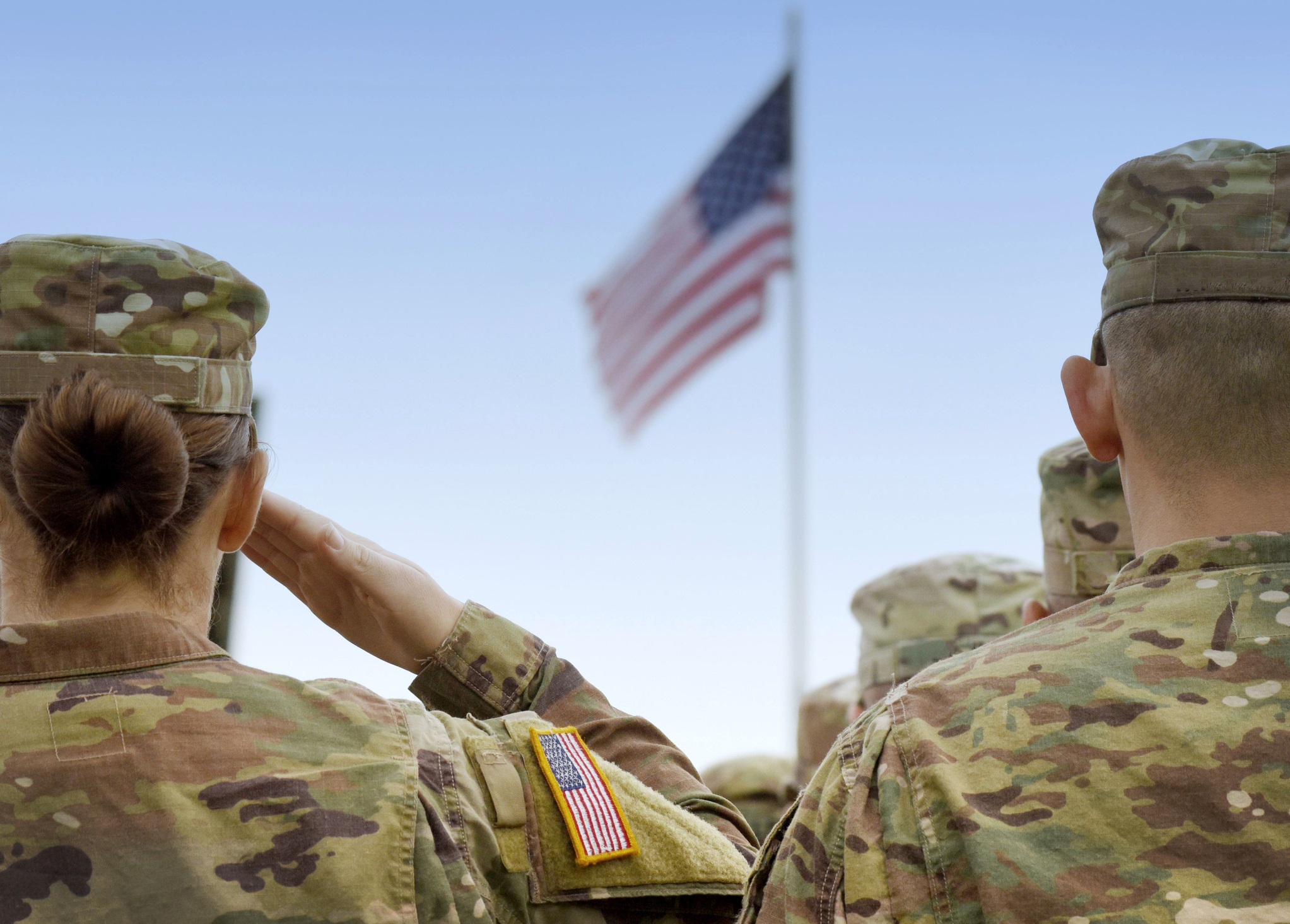 U.S. soldiers are shown from behind saluting a U.S. flag.