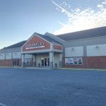 A view of the Cocoaplex cinema, a one-story brick building. Clouds in a blue sky are visible behind it.
