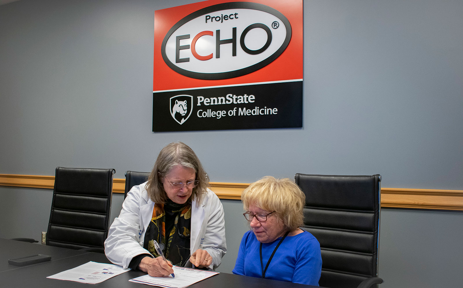Two women sit at a table working with a Project ECHO logo on the wall behind them.