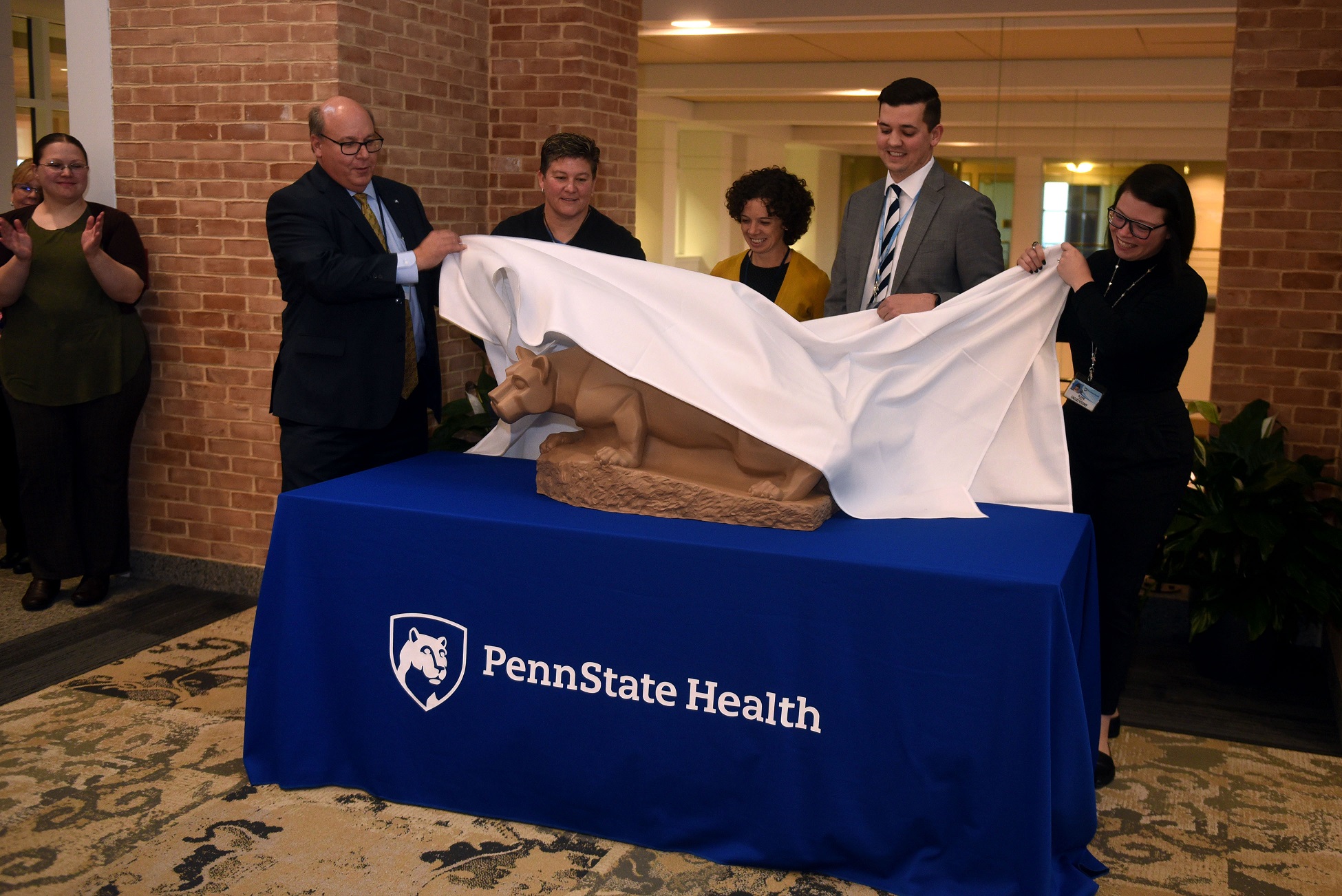 Five people pull a cloth to reveal a statue of a lion.