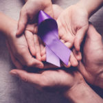 A close-up of three pairs of overlapping hands with a purple, curved ribbon placed on top.