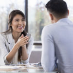 A woman smiles across an office table at a man.