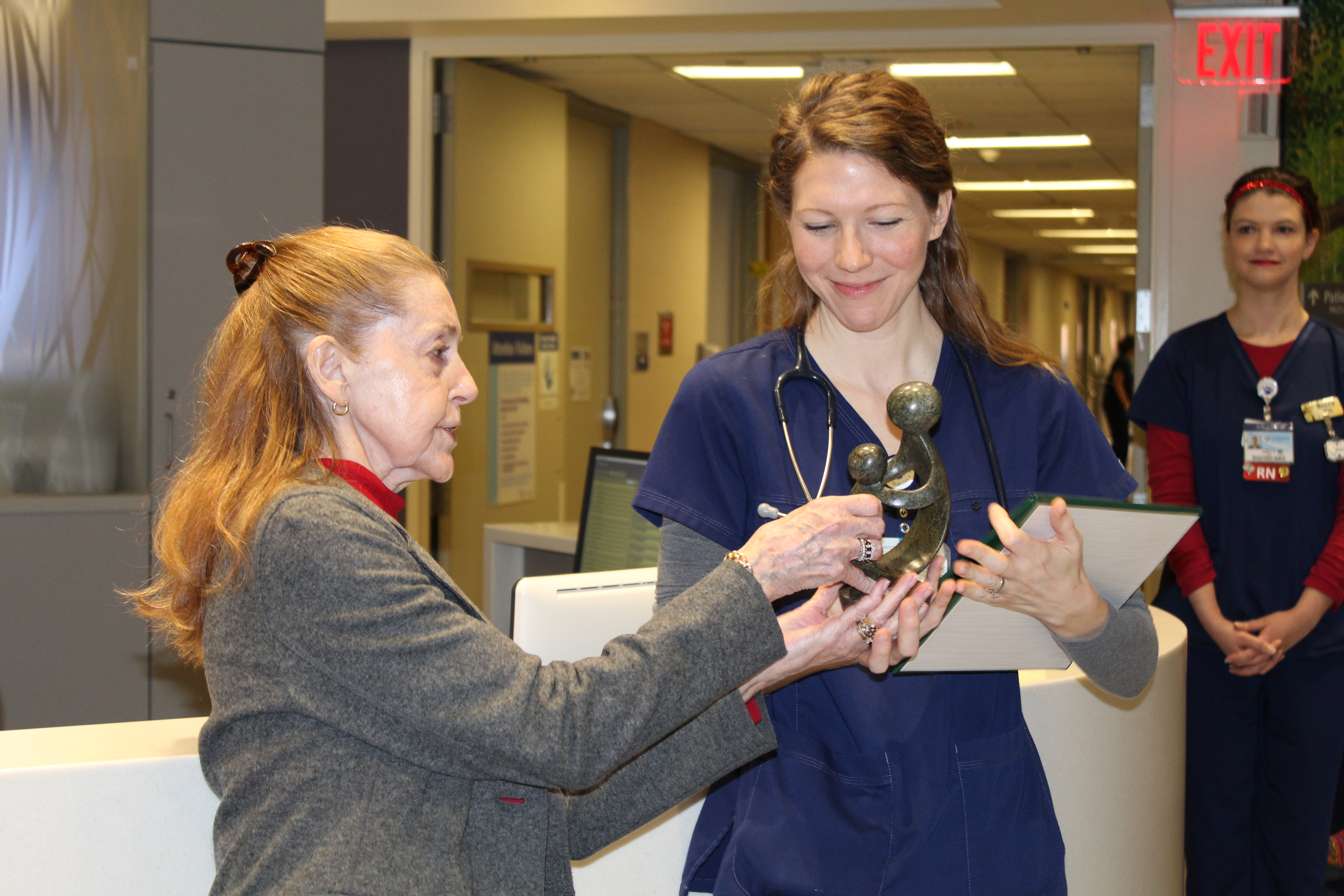 Christine Ewing hands a statue to Elizabeth Etter, who holds a plaque and wears scrubs.