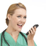: A woman in medical scrubs talks into a smart phone.