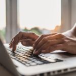 Hands type on the keyboard of a laptop.