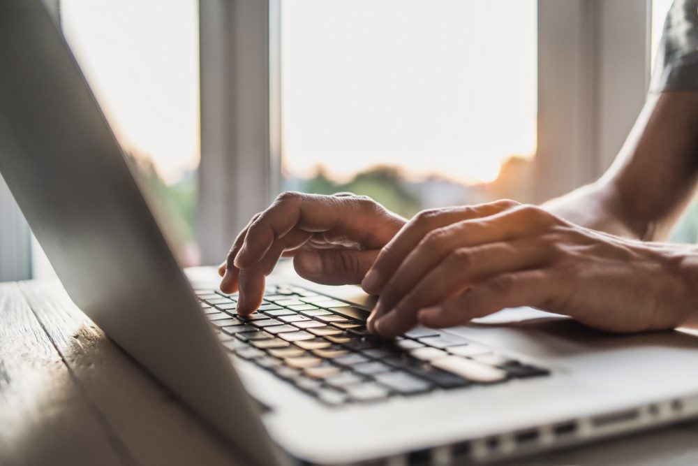 Hands type on the keyboard of a laptop.