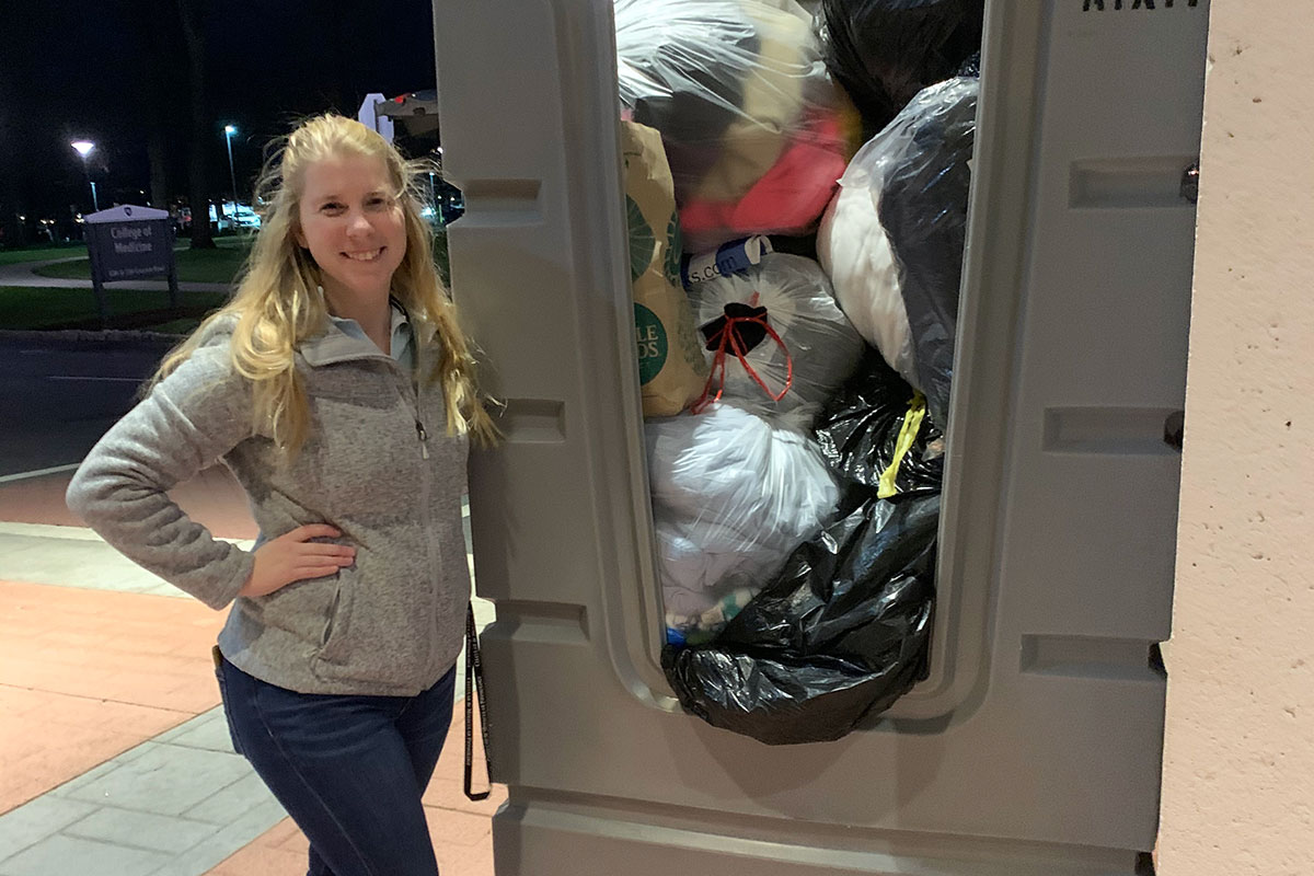 A young woman stands next to a large bin full of bags of winter coats.