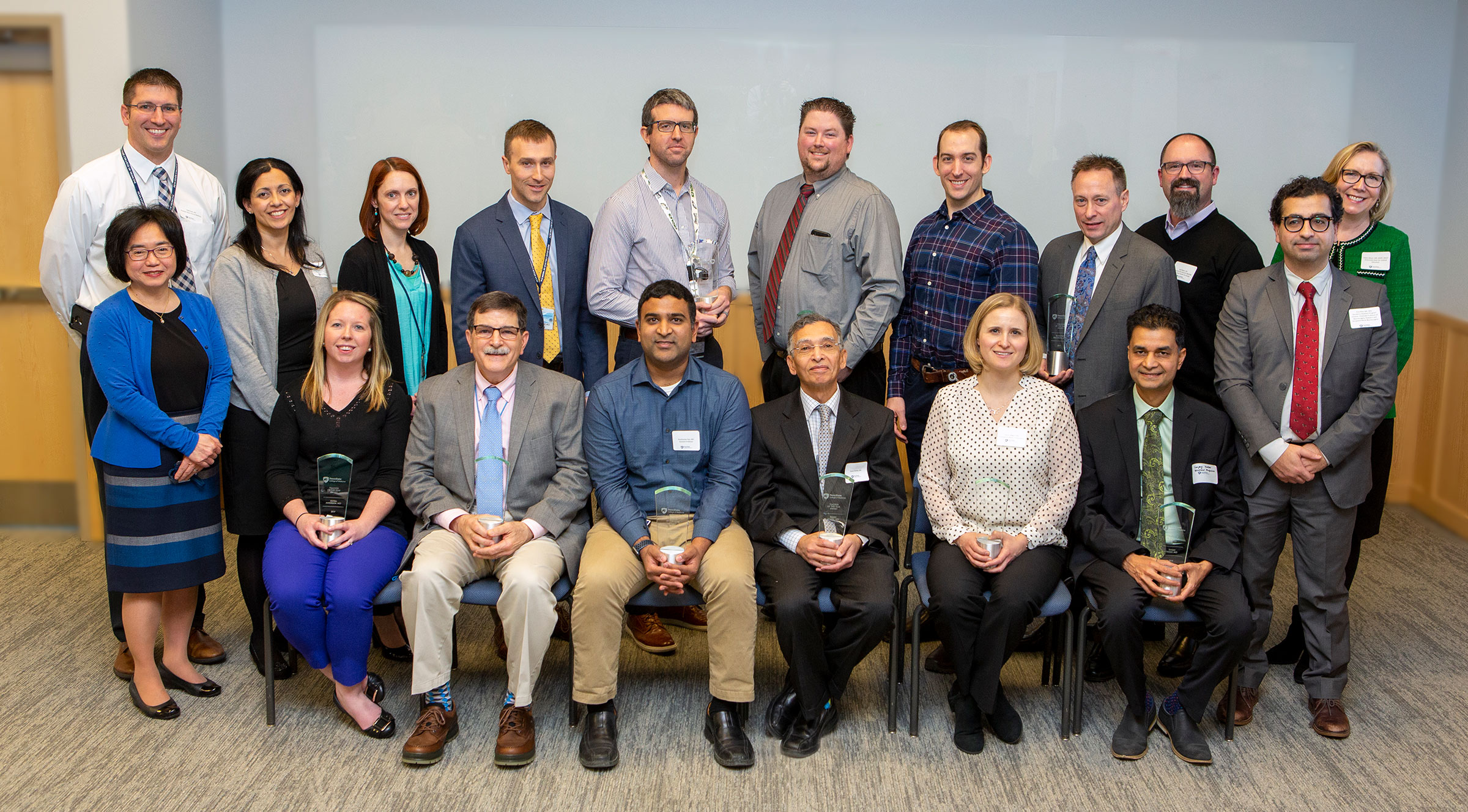 A group of 18 people is seen in two rows - one sitting, one standing. They are the Teacher of the Year award recipients.