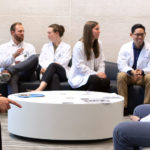 Students in the accelerated (3+) MD pathways at Penn State College of Medicine are pictured in 2019 seated in the lobby of the college on modern-looking chairs. An oblong coffee table is in front of the students. Pictured are, from left, Seth Martin, FM-APPS; Frank Striale, FM-APPS; Dennis Madden, NS-APPS; Elizabeth Zimmerman, IM-APPS; Shannon Brumbaugh, FM-APPS; Alexander Lee, EM-APPS; and Abdel Mohamed, FM-APPS.