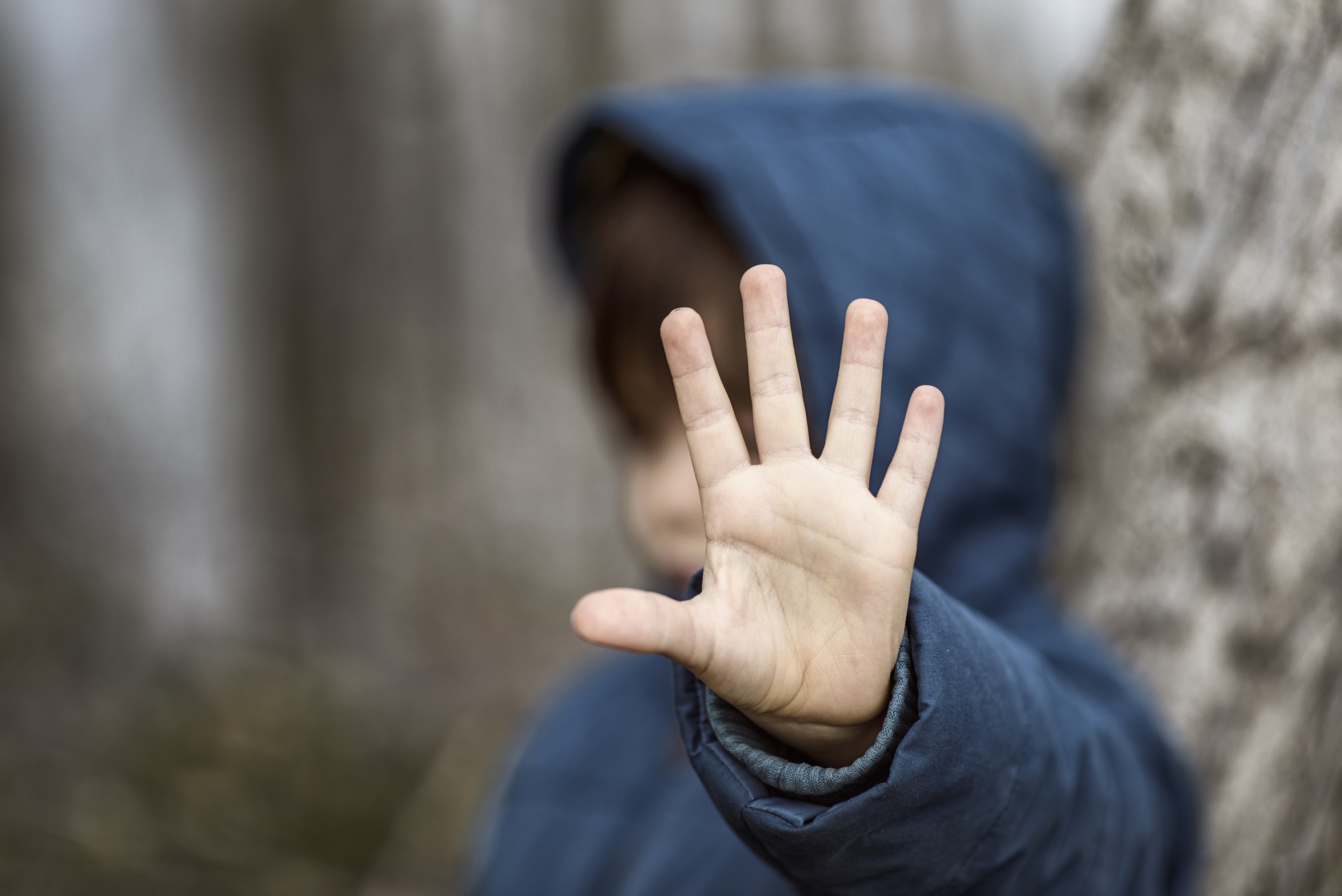 A child wearing a sweatshirt with a hood is seen out of focus and puts his hand up toward the camera.