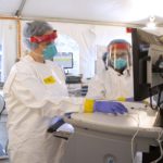 Health care workers wear protective gear and work in a tent.
