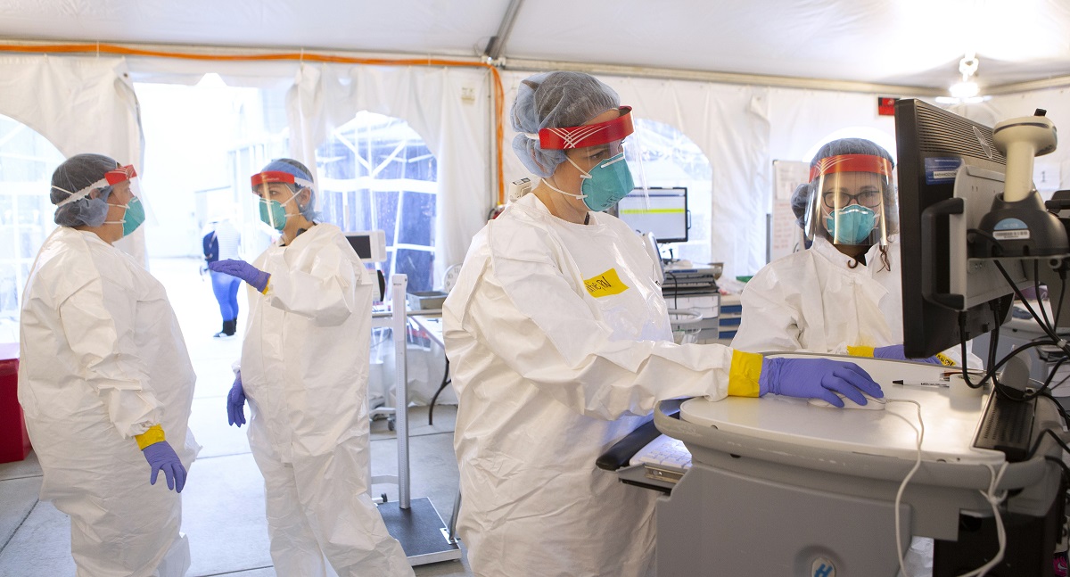 Health care workers wear protective gear and work in a tent.