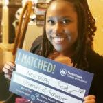 A woman smiles as she holds up a sign that reads: I matched! Neurology; University of Rochester