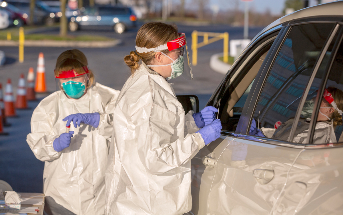 Two nurses wearing personal protective gear administer a car side test for COVID-19