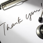 A pen writes the words “Thank You” on coarse paper.