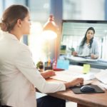 A person on a screen participates in a meeting with people at a conference room.