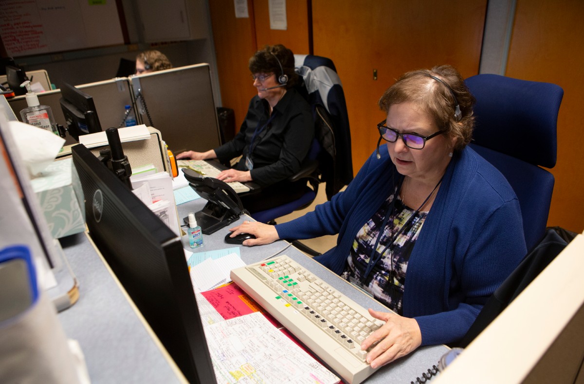 Elaine Allen, foreground, a telephone operator at Hershey Medical Center, sits at a computer wearing a headset and types on a keyboard. Behind her are two other operators.